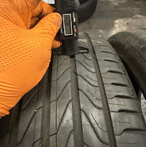 A gloved hand holding a tread depth gauge against a tyre